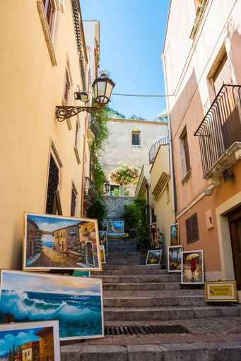 Vertical shot of paintings on street stairs with a blue sky in the background, Taormina, Sicily, Italy
