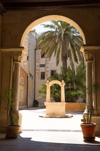 A vertical shot of the stone well city on the street with palm trees in the background. Sicily, Italy.
