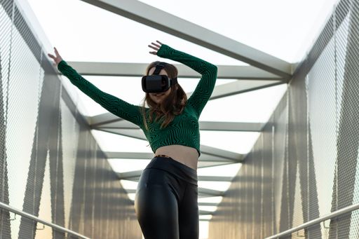 A charming cheerful young woman dancing and wearing a VR box on the street