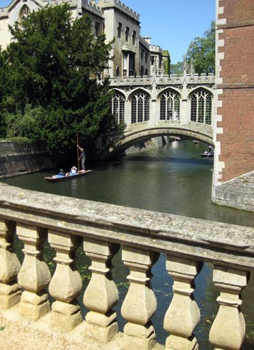 A vertical shot of an old European building with a river flowing around and people sailing in the river