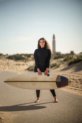 A vertical shallow focus shot of a European female holding a surfboard and standing in the middle of a road