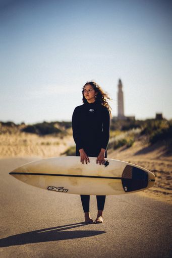 A vertical shallow focus shot of a European female holding a surfboard and standing in the middle of a road