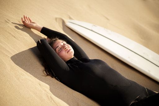 A shallow focus shot of a young European surfer lying on a sandy beach