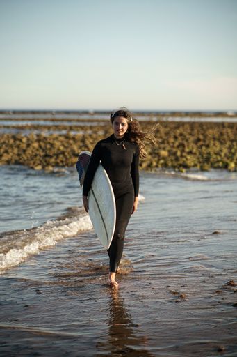 A young beautiful surfer female on the beach at sunset