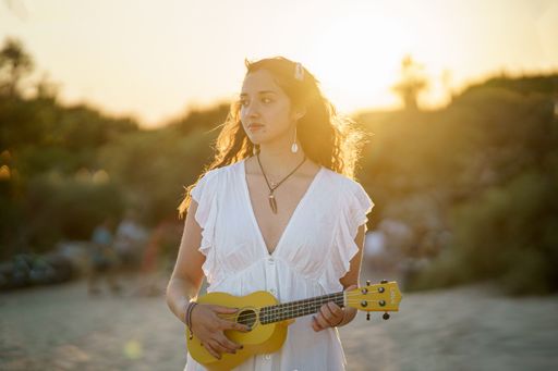 A shallow focus shot of a young European female playing ukulele on a sandy beach