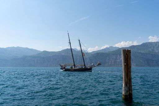 A beautiful shot of a ship sailing in the Lake Garda in bright sunlight against mountains and blue sky in the background, Italy