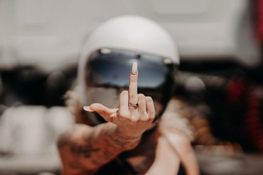 A cool rebellious motorcyclist girl in a helmet with tattoos showing middle finger