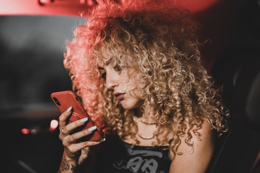 A shallow focus shot of a Caucasian female with blonde curly hair using her phone in the car