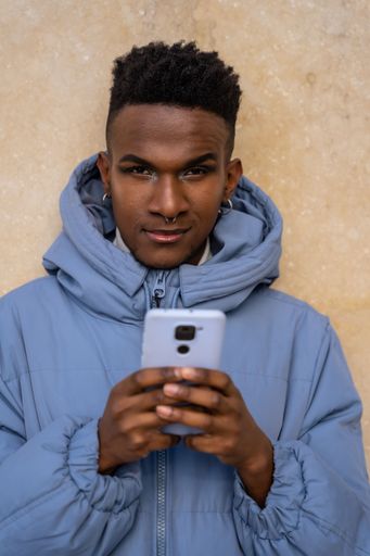 A closeup of a black ethnic man with a phone and a blue jacket on a yellow background