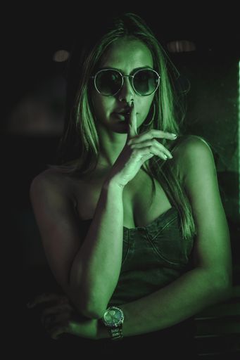 A shallow focus shot of a beautiful Caucasian woman wearing a strapless dress and sunglasses, holding a finger on her lips