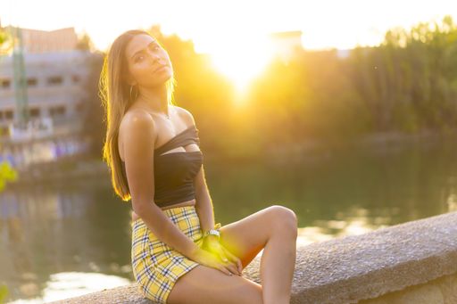A shallow focus shot of a young blonde Caucasian female in a black crop top and yellow plaid skirt in a park during the sunset