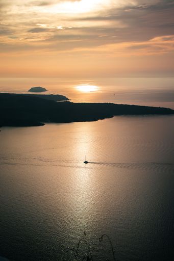 A vertical shot of a beautiful sunset near Firostefani with a sailboat in the sea, Santorini, Greece