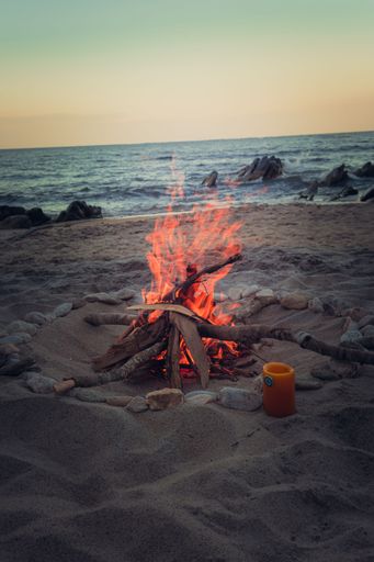 A vertical shot of a small camp fire on the beach by the water and a sunset sky in Lake Malawi, Africa