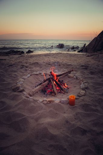A bonfire on a sandy beach with a beautiful sunset background