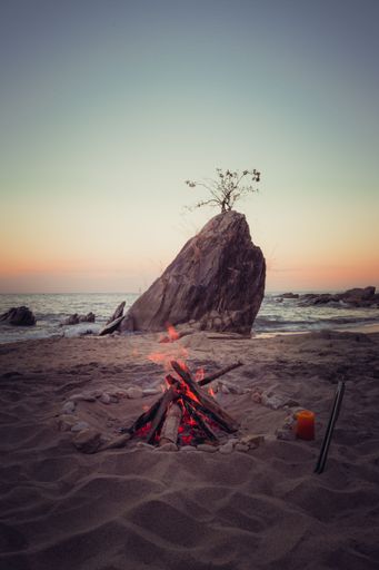 A vertical shot of a big rock and camp fire on the beach by the water and a sunset sky in Lake Malawi, Africa