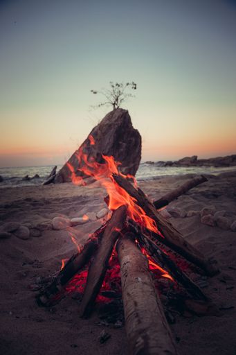 A vertical shot of a big rock and camp fire on the beach by the water and a sunset sky in Lake Malawi, Africa