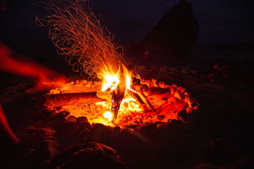 A vertical shot of a small camp fire on the beach by the water and a sunset sky in Lake Malawi, Africa