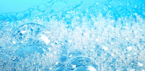 A closeup of transparent bubbles of soap foam covering surface of bright blue water