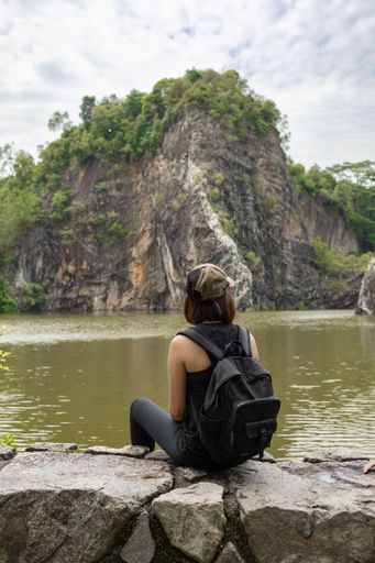 A rear view of a female looking the cliff view while sitting on a rock in Singapore