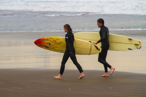 A view of a couple in wetsuits with surfing boards on the beach getting ready to surf