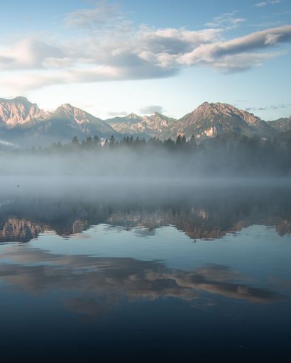 A vertical shot of a foggy lake with high mountains in the background