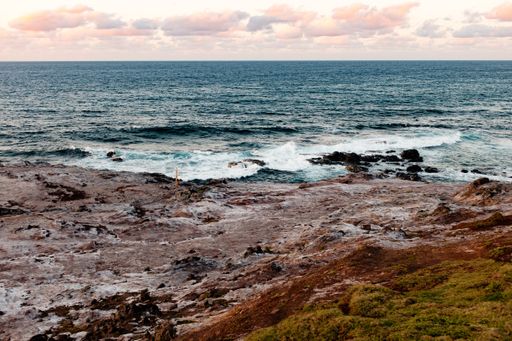 A landscape shot of a body of water near a rocky shore with waves splashing the rocks. Perfect for a wallpaper or a background.
