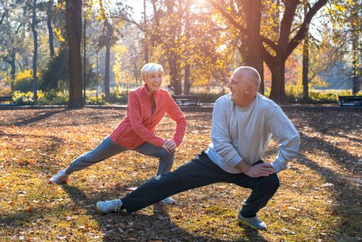 Smiling senior couple exercise together in the park in autumn