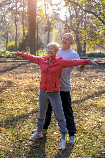 A senior male and a female exercising together in the park in autumn