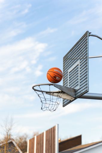 A low-angle shot of a basketball ball falling into the net with a hoop and sky in the background