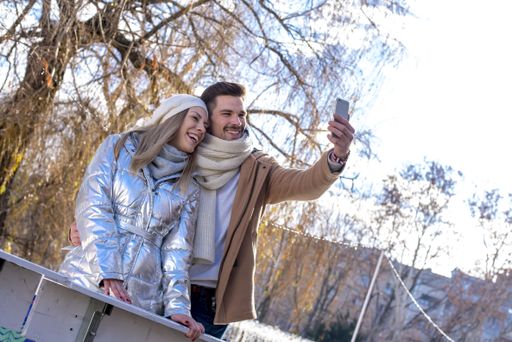 A closeup shot of happy smiling Caucasian couple having fun taking selfies in winter park on a sunny day