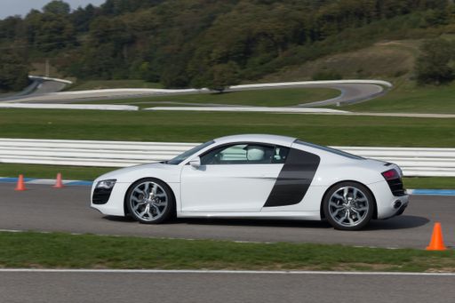 A view of a white Audi R8 sports car on an asphalt road against a green lawn on a sunny day