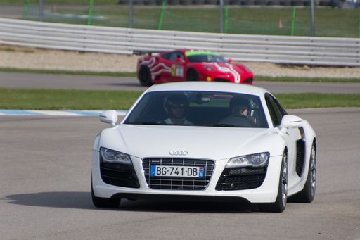 A view of a white Audi R8 sports car on an asphalt road against a green lawn on a sunny day