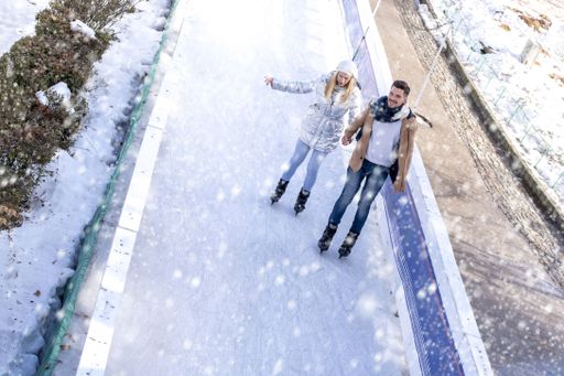 A young beautiful Caucasion couple ice skating and having fun while enjoying snowfall in winter park