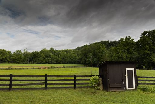 A view of a beautiful green field with the gloomy sky over and a single-storey building near the fence