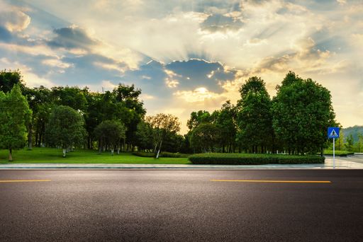 empty asphalt road near park with explosive sunshine in the sky during sunrise.