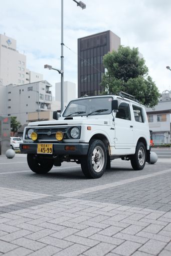 A vertical shot of a white Land Rover Defender on the street near high buildings