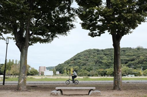 A horizontal shot of a male riding a bicycle on the pathway with high green mountains in the background