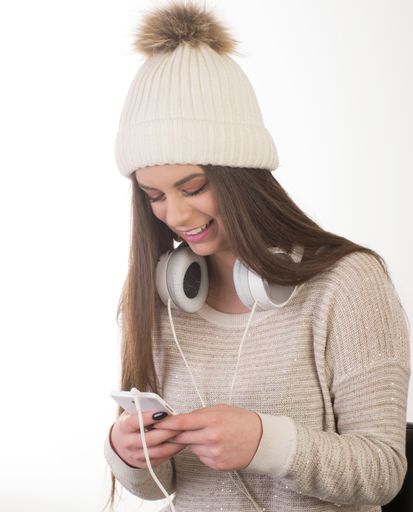 A smiling caucasian female in a sweater and white hat with her headphones and smartphone isolated on a white background