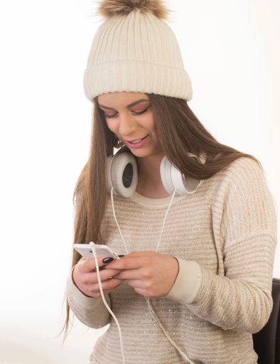 A caucasian female in a sweater and white hat with her headphones and smartphone isolated on a white background