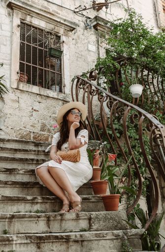 A happy female in a white hat with sunglasses and hat sitting on the stairs