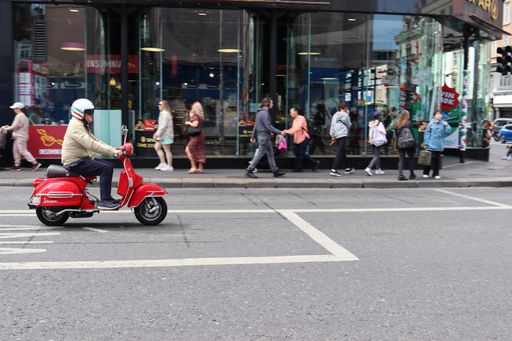 Striking urban scene of a man riding a vibrant red scooter through the streets of Dublin, Ireland