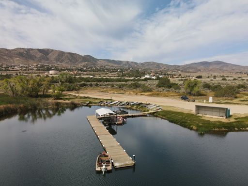 A wooden dock on the Lake Palmdale surrounded by mountains against a cloudy sky