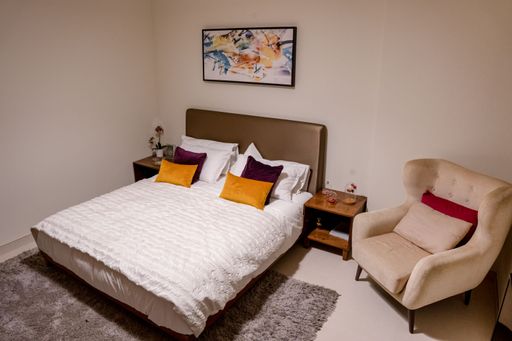 A small bedroom with a bed, nightstand and chair in a minimal style