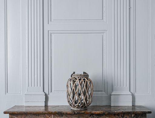 A vase made of thin metal lines behind the white wall