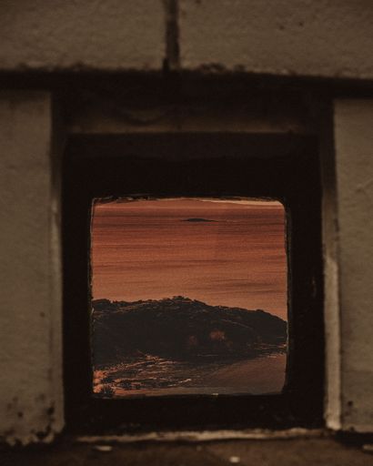 A vertical shot of a view of the sea from a brick abandoned building window with orange tint
