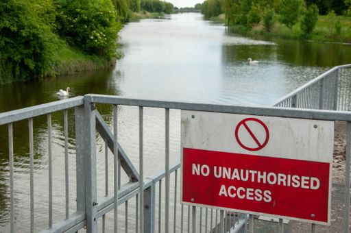 A sign on the metal railings behind the water in the park prohibiting unauthorized access