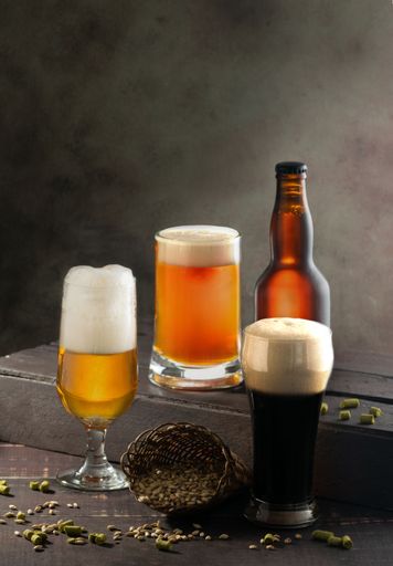 A vertical shot of different glasses with foamy beer and a bottle of beer