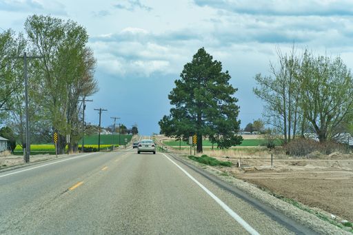 Two cars on the U.S. 95 asphalt highway in Southern Idaho under a blue sky with large clouds