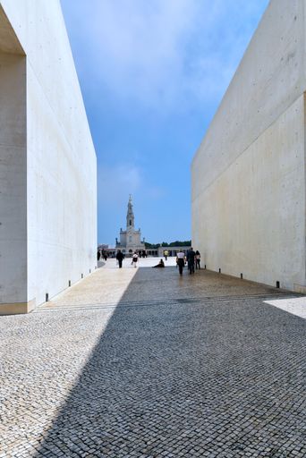 A vertical shot of an alley surrounded by white buildings in blue sky background in Fatima, Portugal