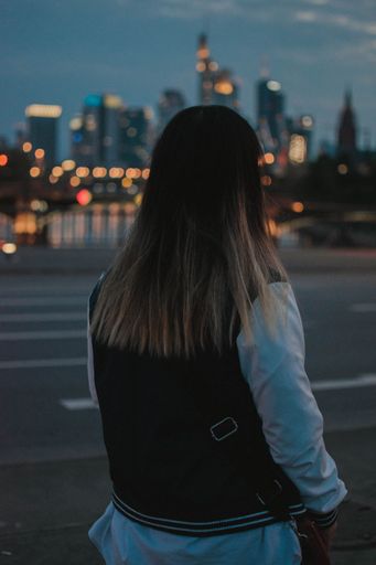 A back view of a female on a street looking at the city in the evening